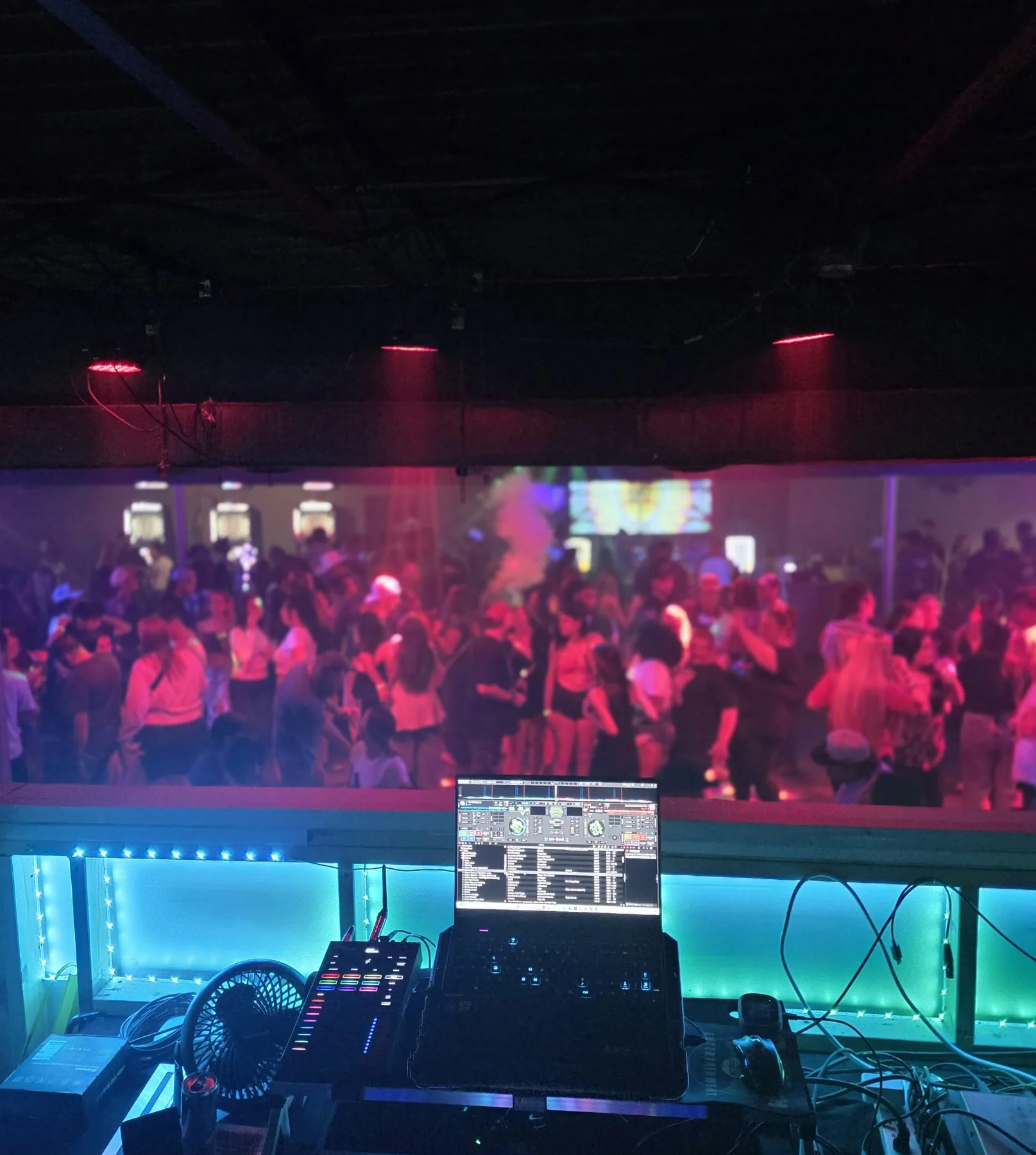 View from the DJ booth over a red-lit dance floor
