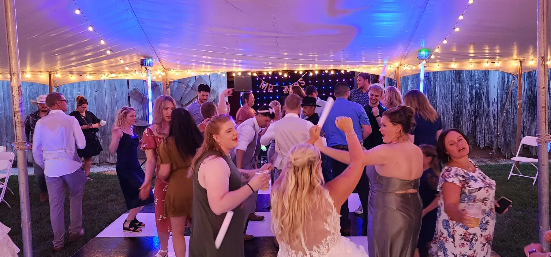 Wedding guests dancing under string lights in an outdoor tent